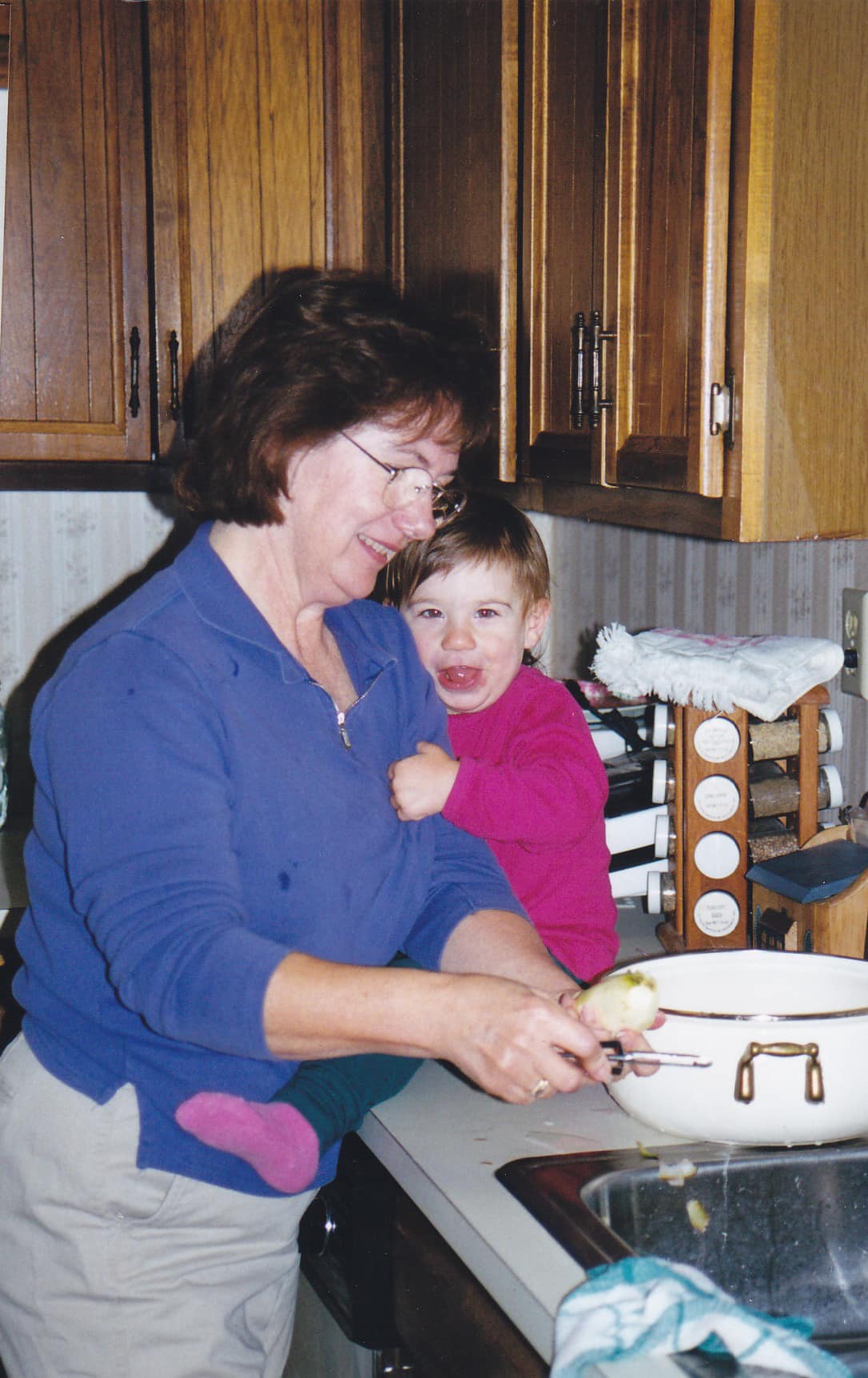 My grandma holds me, as a baby, on the counter while peeling potatoes