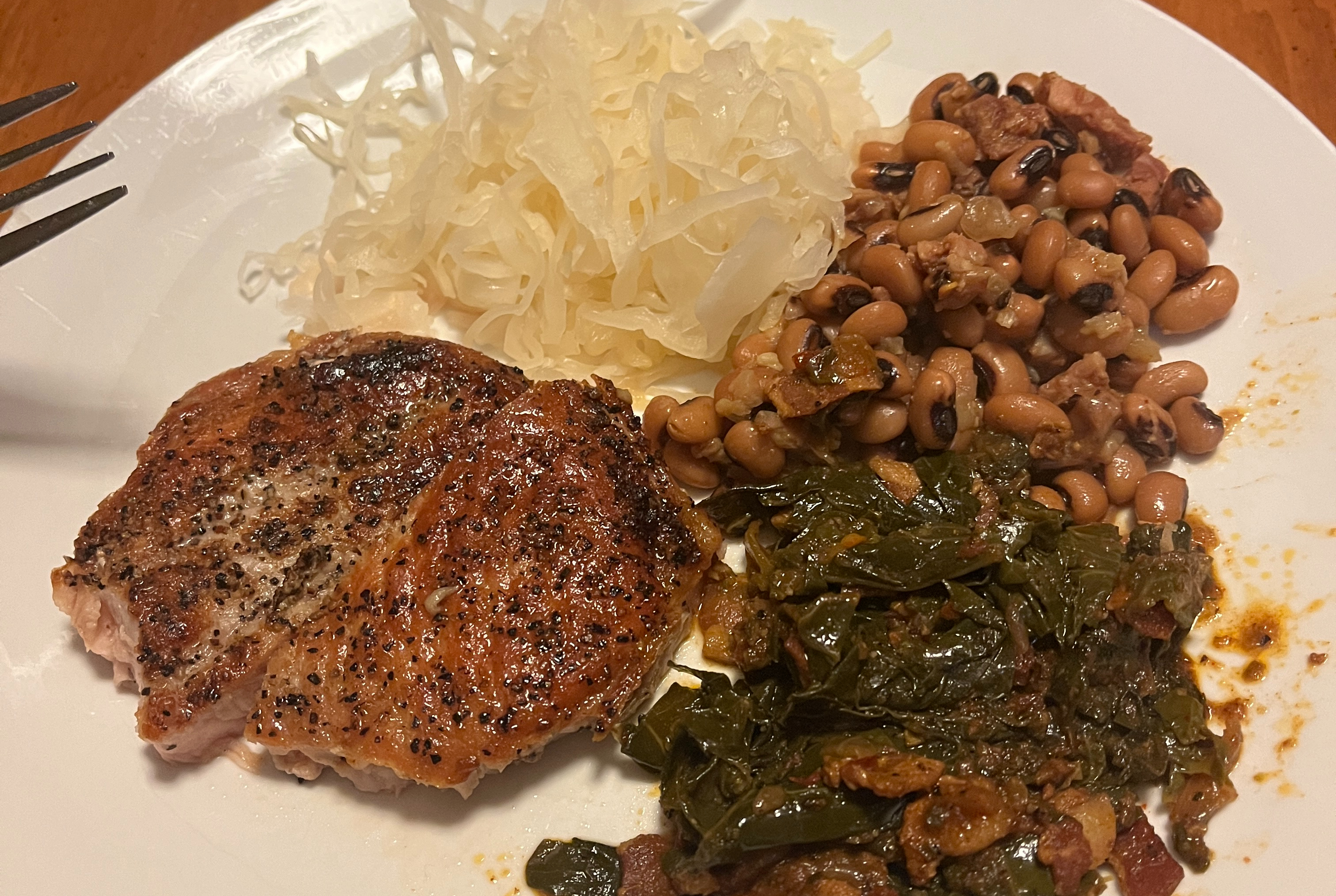 seared pork chop, sauerkraut, black eyed peas and collard greens on a white plate